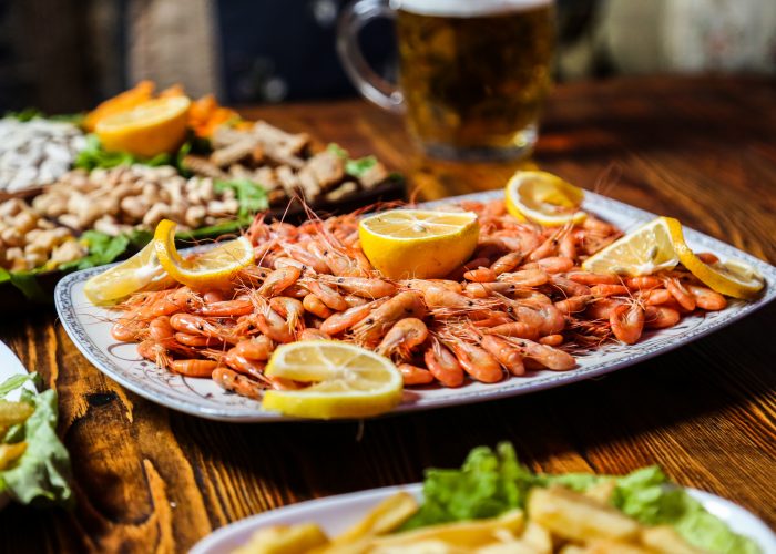 side view boiled shrimp with lemon wedges on a plate with beer snacks and a glass of beer on the table
